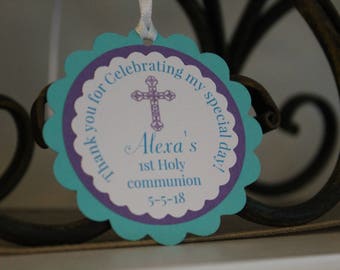 May include: A round tag with a scalloped edge in teal and purple. The tag says "Thank you for Celebrating my special day!" and features a cross and the text "Alexa's 1st Holy communion 5-5-18".
