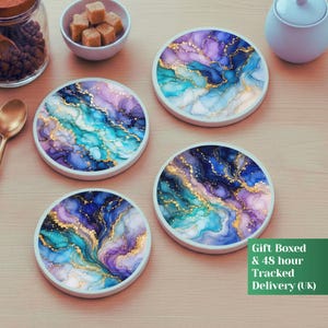 Op de afbeelding: Vier ronde onderzetters met een vloeiend abstract ontwerp met wervelende patronen van diepblauw, levendig turkoois en zachtpaars, geaccentueerd door dunne, glinsterende gouden aders die lijken op natuursteen of marmeren texturen.