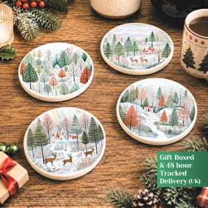 May include: Four round ceramic coasters featuring winter landscape illustrations with snow-covered trees, small houses, and deer. Each coaster displays a unique scene with a colour palette of green, red, white, and brown, set against a wooden surface.
