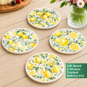 Op de afbeelding: Een set van vier ronde keramische onderzetters met een aquarelpatroon van gele citroenen, groene bladeren en witte bloesems. Elke onderzetter toont een herhalend botanisch ontwerp met heldere citrusvruchten en bladeren.