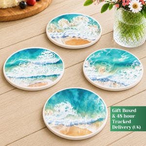 May include: Four round coasters featuring a printed design of ocean waves crashing onto a sandy beach. Each coaster displays a vibrant blue and turquoise sea with white foam patterns and a tan shoreline, arranged on a light wood surface.
