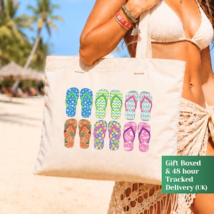 May include: A beige canvas tote bag featuring a graphic print of ten colorful flip-flops arranged in two rows. The flip-flops display various patterns including stars, chevrons, floral motifs, and geometric shapes in shades of blue, green, and pink.