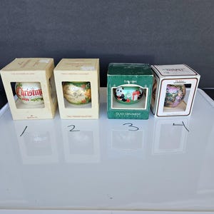 May include: Four vintage Christmas ornaments in their original boxes. The ornaments feature various designs, including text and illustrations. The boxes are in different colors, with text such as "Christmas 1979" and "Baby's First Christmas".