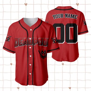 Op de afbeelding: Rood honkbalshirt met zwarte afwerking en witte knopen. De voorkant toont het woord "DEADPOOL" in een vetgedrukte, omlijnde letter, samen met het Deadpool-logo. De achterkant heeft de tekst "YOUR NAME" boven het nummer "00".