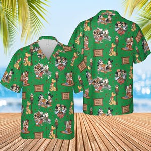 May include: Green button-up shirt featuring a repeating pattern of Mickey Mouse, Minnie Mouse, Pluto, and other Disney characters. The shirt has a tropical design with the words "HOME SWEET HOME" on signs throughout the pattern. The shirt is short-sleeved.