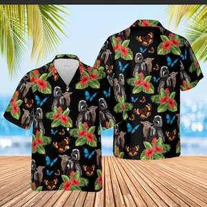 May include: Black Hawaiian shirt featuring a repeating pattern of a Mandalorian character, a small green creature, red hibiscus flowers, and butterflies. The shirt has short sleeves and a button-down front.