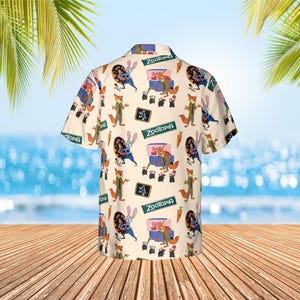 May include: Cream-colored button-down shirt featuring a repeating pattern of characters and elements from the animated film Zootopia. The design includes images of a fox, a rabbit, a carrot, and the film's logo. The shirt has short sleeves.