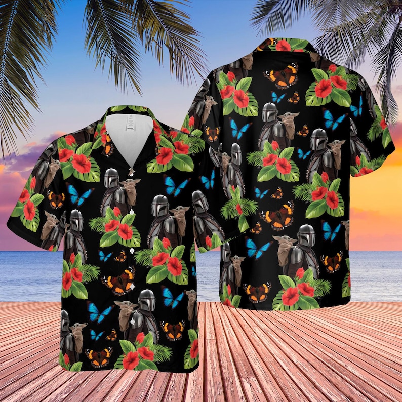 May include: Black short-sleeve button-down shirt with a tropical design. The shirt features a repeating pattern of a Mandalorian character, a small green creature, red hibiscus flowers, and butterflies. The shirt is on a wooden deck with a beach and sunset background.