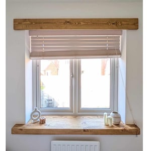 May include: A window featuring a wooden frame and shelf. The window has a light-coloured blind and a white frame. Decorative items, including a vase and candles, are on the shelf. The wood has a natural grain.