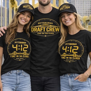 May include: Three people wearing black t-shirts and baseball caps with the text "PITTSBURGH DRAFT CREW". The shirts feature a gold clock design with the text "YINZ ON THE CLOCK" and the year "2026 DRAFT".