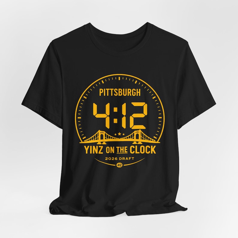 May include: Black t-shirt with a gold graphic. The graphic features the word "Pittsburgh" above the numbers "4:12" in a clock-like design. Below the numbers is "Yinz on the Clock" and "2026 Draft".