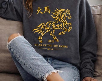 May include: Dark gray sweatshirt featuring a golden yellow illustration of a horse with the text "Year of the Fire Horse 2026" and Chinese characters. The sweatshirt is a crew neck style.