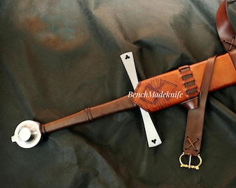 May include: A medieval sword with a brown leather-wrapped handle and a silver pommel. The sword is sheathed in a brown leather scabbard with decorative tooling. A brown leather strap with a gold-coloured buckle is attached.