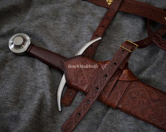 May include: A medieval sword with a brown leather handle and sheath. The sheath and belt have detailed embossed patterns. The sword's blade is silver, and the handle has a silver pommel. The text "BenchMadeknife" is visible on the sheath.