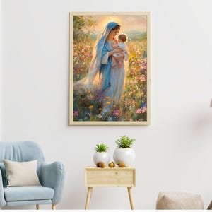 May include: A framed art print depicts a woman in a blue robe holding a child in a field of colorful flowers. The artwork has a soft, painterly style with warm lighting, creating a serene and spiritual atmosphere. The frame is a light wood color.