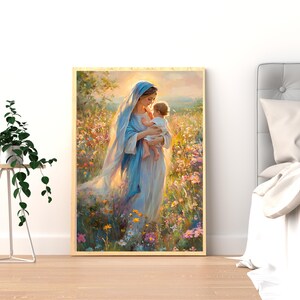 May include: A framed art print depicts a woman in a blue robe holding a baby. The artwork is set in a field of colorful wildflowers, with soft lighting and a warm color palette. The print is displayed on a wooden floor.