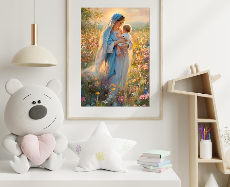 May include: A framed print depicts a woman in a blue robe holding a baby in a field of flowers. The artwork has a soft, painterly style with warm lighting. The frame is a light wood color, and the print is displayed in a room with a white shelf and decorative items.