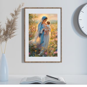 May include: A framed art print depicts a woman in a blue veil holding a baby in a field of flowers. The artwork has a soft, painterly style with warm, golden light. The frame is a light brown color.