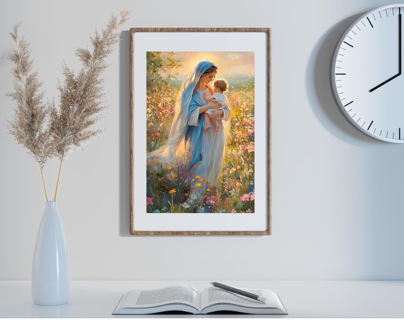 May include: A framed art print depicts a woman in a blue veil holding a baby in a field of flowers. The artwork has a soft, painterly style with warm, golden light. The frame is a light brown color.