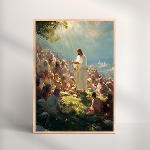 Op de afbeelding: Een ingelijste prent toont een religieuze scène met een centrale figuur in witte gewaden die een grote menigte toespreekt. Het kunstwerk heeft zachte verlichting, met lichtstralen die naar beneden schijnen. De scène speelt zich buiten af met een heuvel en een blauwe lucht.