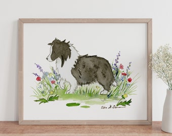 May include: Watercolor painting of a dog in a wooden frame. The dog is black and white, sitting in a field of wildflowers. The artwork is signed in the bottom right corner. A white vase with flowers sits on a wooden table.