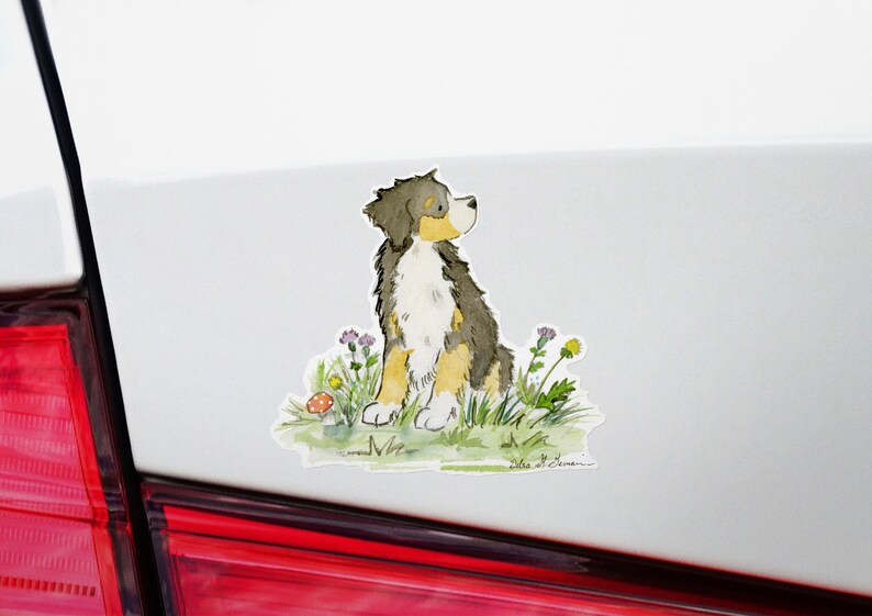 May include: A watercolor illustration of a Bernese Mountain Dog sitting in a field of wildflowers. The dog is looking up and has a brown, black, and white coat. The background is a light blue sky.