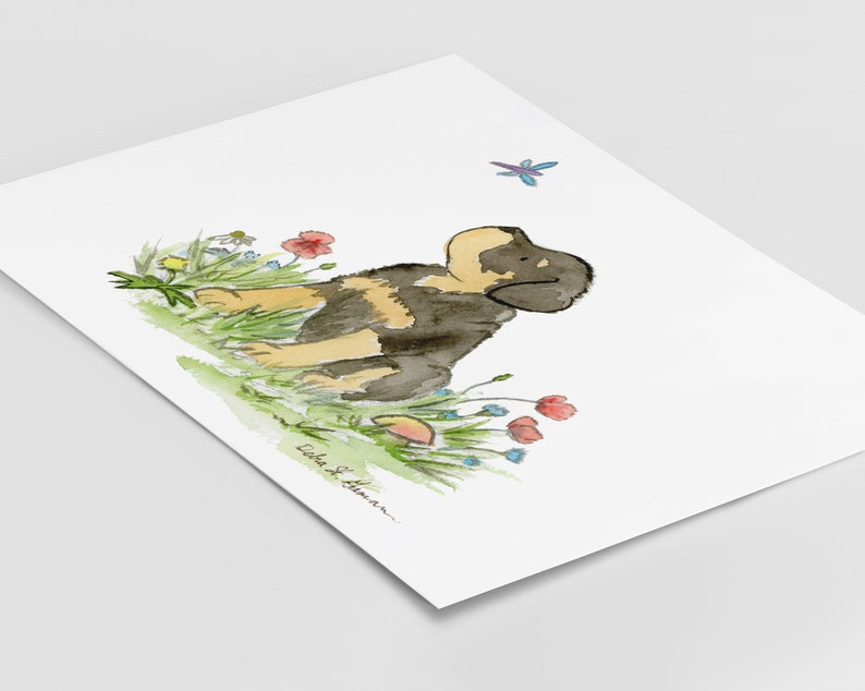 May include: Watercolor painting of a black and brown puppy sitting in a field of flowers. The puppy is looking to the right and there is a dragonfly flying above it. The painting is signed "Lida S. Hamar".