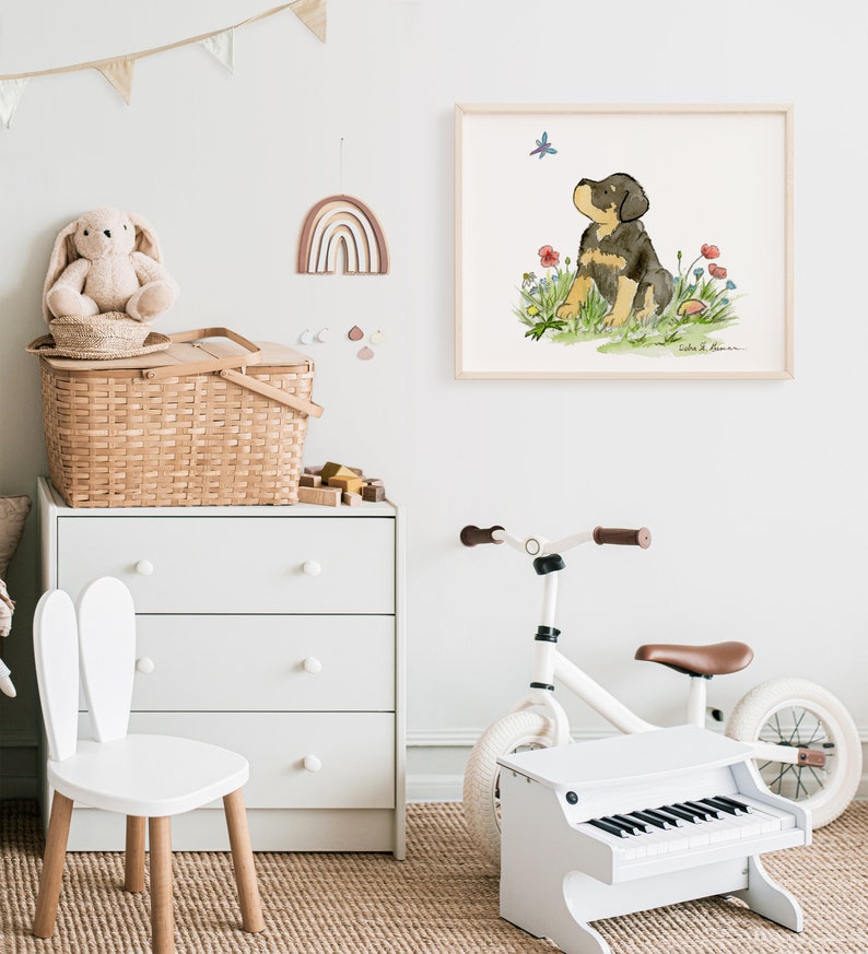 May include: A watercolor illustration of a black and brown puppy sitting in a field of flowers, looking up at a butterfly. The illustration is framed and hanging on a white wall in a nursery.
