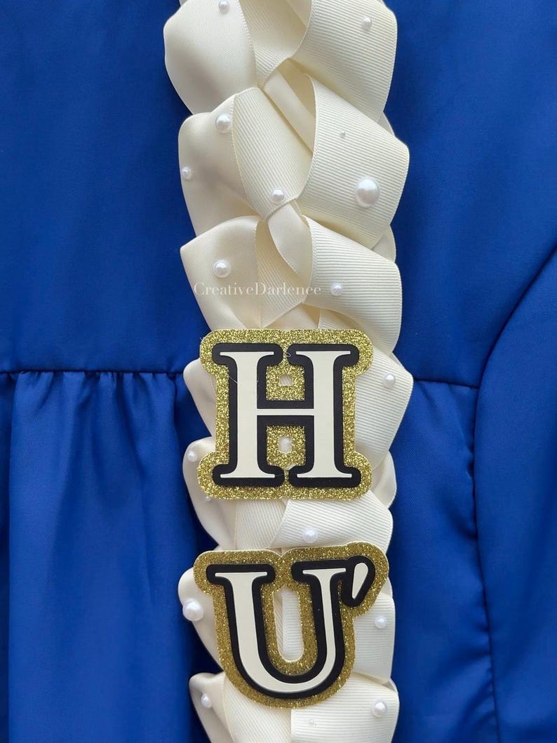 K&ouml;nnte beinhalten: Ein cremefarbenes Band-Lei mit den Buchstaben "H" und "U" in goldfarbenem Glitzer und schwarzem Rand. Das Lei ist mit kleinen, wei&szlig;en Perlen verziert und vor blauem Hintergrund platziert. Der Text "CreativeDarlence" ist sichtbar.