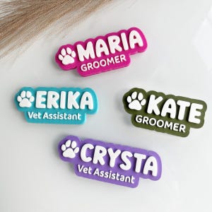 Peut inclure: Quatre badges nominatifs personnalisés avec une icône de patte et des lettres blanches en relief. Les badges sont magenta, bleu sarcelle, vert olive et violet, affichant les noms Maria, Erika, Kate et Crysta, ainsi que leurs titres professionnels.
