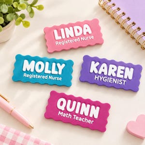 Peut inclure: Quatre badges nominatifs rectangulaires aux bords festonnés en rose, bleu, violet et magenta. Chaque badge présente des lettres blanches en relief affichant les noms LINDA Registered Nurse, MOLLY Registered Nurse, KAREN HYGIENIST et QUINN Math Teacher.