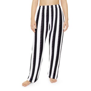 May include: Black and white striped pajama pants. The pants have vertical stripes and a repeating script pattern down the black stripes. The pants are made of a soft, flowing material.