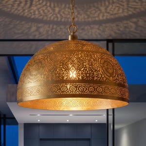 Peut inclure: Une suspension en forme de dôme en métal doré présentant des motifs complexes découpés au laser qui créent des perforations détaillées sur toute la surface. Le luminaire est suspendu par une chaîne dorée assortie et diffuse la lumière.