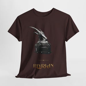 Puede incluir: Camiseta granate con una ilustración en escala de grises de un casco con cuernos. El texto "ILLYRIAN" está impreso en dorado debajo de la imagen, separado por una línea horizontal.