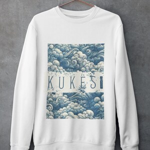 May include: White sweatshirt featuring a blue and white cloud pattern. The design includes the word "KUKESI" in a white rectangular banner. The sweatshirt is hanging on a copper-coloured hanger against a grey wall.