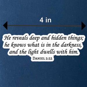 Op de afbeelding: Een marineblauw notitieboek van 21 x 14 cm, met een witte sticker met de tekst "He reveals deep and hidden things; he knows what is in the darkness, and the light dwells with him. DANIEL 2:22."