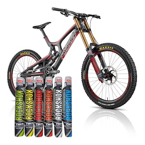 Puede incluir: Una bicicleta de montaña negra y roja con horquillas de suspensión doradas y neumáticos Maxxis. Se muestran seis protectores de horquilla Rockshox de varios colores frente a la bicicleta, cada uno con el logotipo de Rockshox.