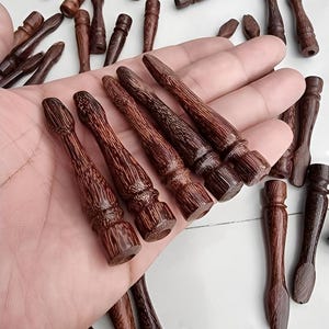 May include: A collection of small, intricately carved wooden objects in varying shades of brown. Several are held in a hand, showcasing their detailed craftsmanship. The objects appear to be decorative or functional, possibly for crafts or home decor.
