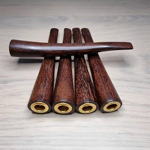 Op de afbeelding: Een verzameling van vijf donkerbruine houten pijpenstelen met een gepolijste afwerking, gerangschikt in een waaier. Elke steel heeft een conische body en een goudkleurige metalen ring aan de basis. Een gebogen mondstuk rust erbovenop.