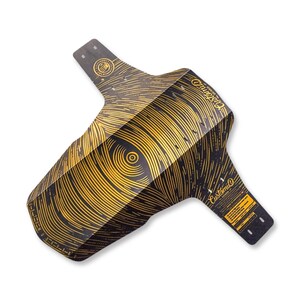 Peut inclure: Un garde-boue de vélo noir avec un motif de lignes circulaires dorées rayonnant depuis un point central. Le garde-boue porte le texte CustomiD Guard et divers petits détails techniques imprimés en or, avec plusieurs trous de fixation.