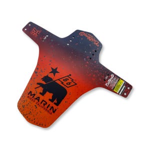 May include: A bicycle mudguard with a red and blue gradient, featuring a black bear holding a flag with the number 86. The text "Marin Bikes California" is printed below the bear. The mudguard has a splatter design.