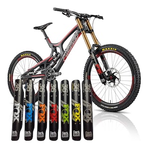 Puede incluir: Una bicicleta de montaña negra y roja con horquillas de suspensión doradas y neumáticos negros. La bicicleta tiene la marca "Santa Cruz" en el cuadro. Siete protectores de horquilla negros con el logotipo "FOX" y "36" están delante de la bicicleta.