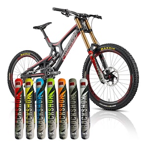Könnte beinhalten: Ein schwarzes und rotes Mountainbike mit goldenen Federgabeln und schwarzen Reifen. Sieben farbige "ROCKSHOX" Gabelprotektoren werden vor dem Fahrrad angezeigt. Das Fahrrad hat den Text "SANTA CRUZ" auf dem Rahmen.