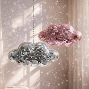 May include: Two cloud-shaped disco ball pendant lights hang from the ceiling. One is silver, the other is pink. The lights are suspended by chains and reflect light onto the walls and bed below. The room has a soft, dreamy aesthetic.