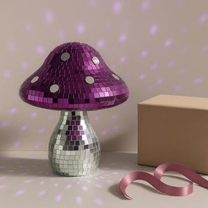 Pu&ograve; includere: Lampada decorativa a forma di fungo con cappello a mosaico viola e base a mosaico argentata. La lampada &egrave; accanto a una scatola avvolta e un nastro rosa. Arredamento per la casa.