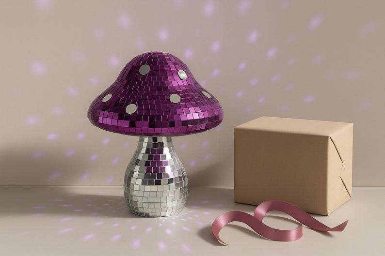 Pu&ograve; includere: Lampada decorativa a forma di fungo con cappello a mosaico viola e base a mosaico argentata. La lampada &egrave; accanto a una scatola avvolta e un nastro rosa. Arredamento per la casa.