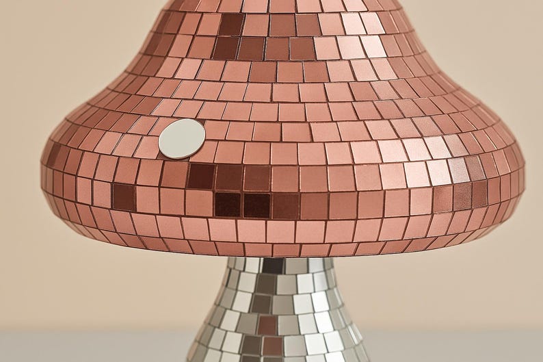 Pu&ograve; includere: Una lampada da tavolo a forma di fungo con un design a mosaico. La parte superiore della lampada &egrave; color rame e la base &egrave; argentata. La lampada ha un dettaglio circolare bianco sul lato.