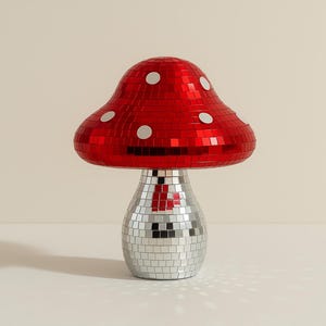 Pu&ograve; includere: Lampada decorativa a forma di fungo con cappello rosso a specchio e base argentata a specchio. Il cappello ha accenti circolari bianchi. La lampada &egrave; su una superficie bianca.