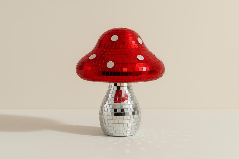 Pu&ograve; includere: Lampada decorativa a forma di fungo con cappello rosso a specchio e base argentata a specchio. Il cappello ha accenti circolari bianchi. La lampada &egrave; su una superficie bianca.