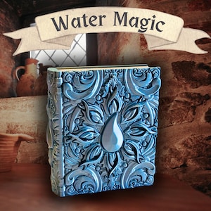 May include: A blue, ornate book with the words "Water Magic" on a banner above it. The book has a detailed, floral design with a central teardrop shape. The background includes a rustic, stone wall and wooden surface.